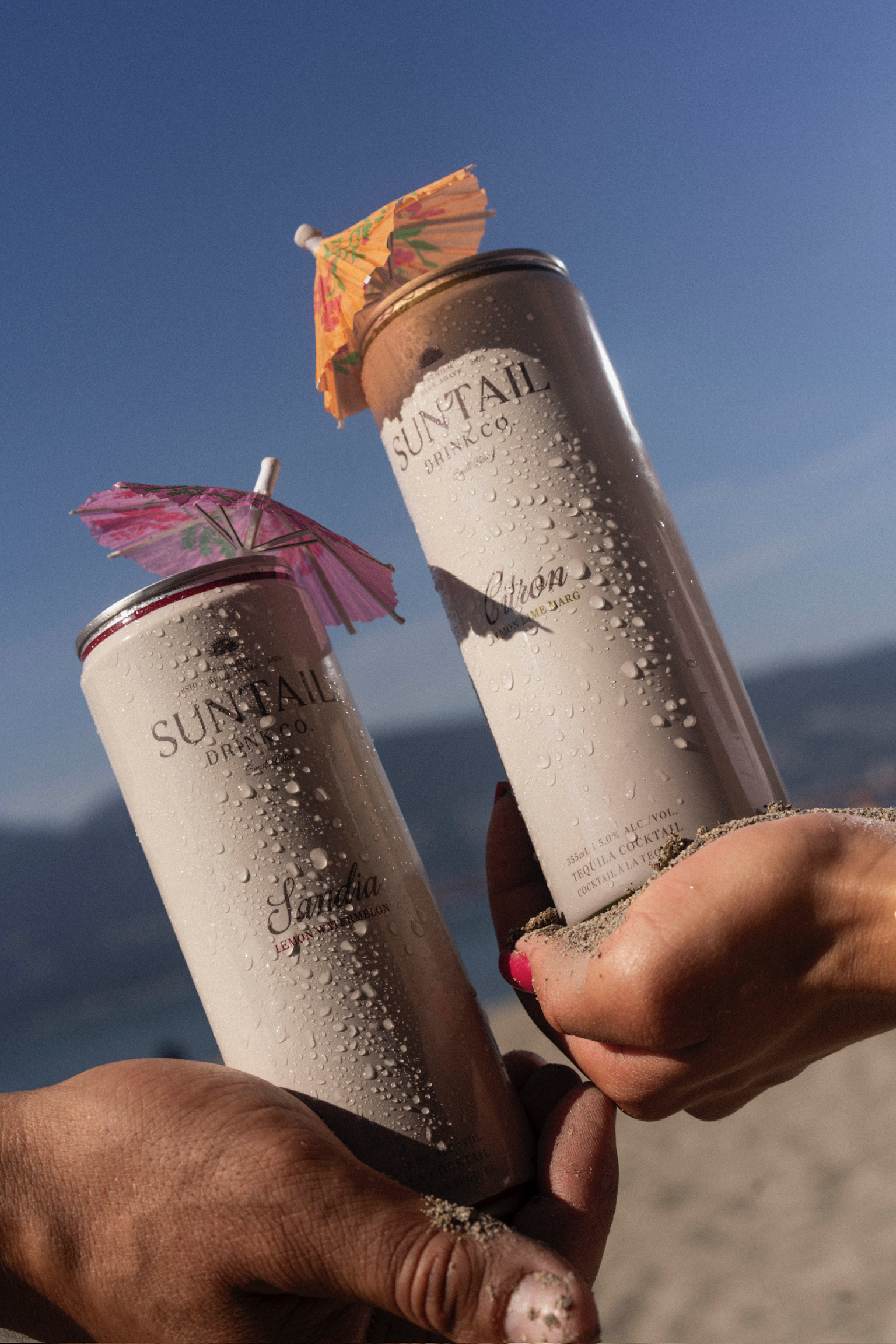 Hand removing a Suntail Drink Co. Sandia lemon watermelon canned tequila cocktail from a refrigerator door shelf with three other identical cans.
