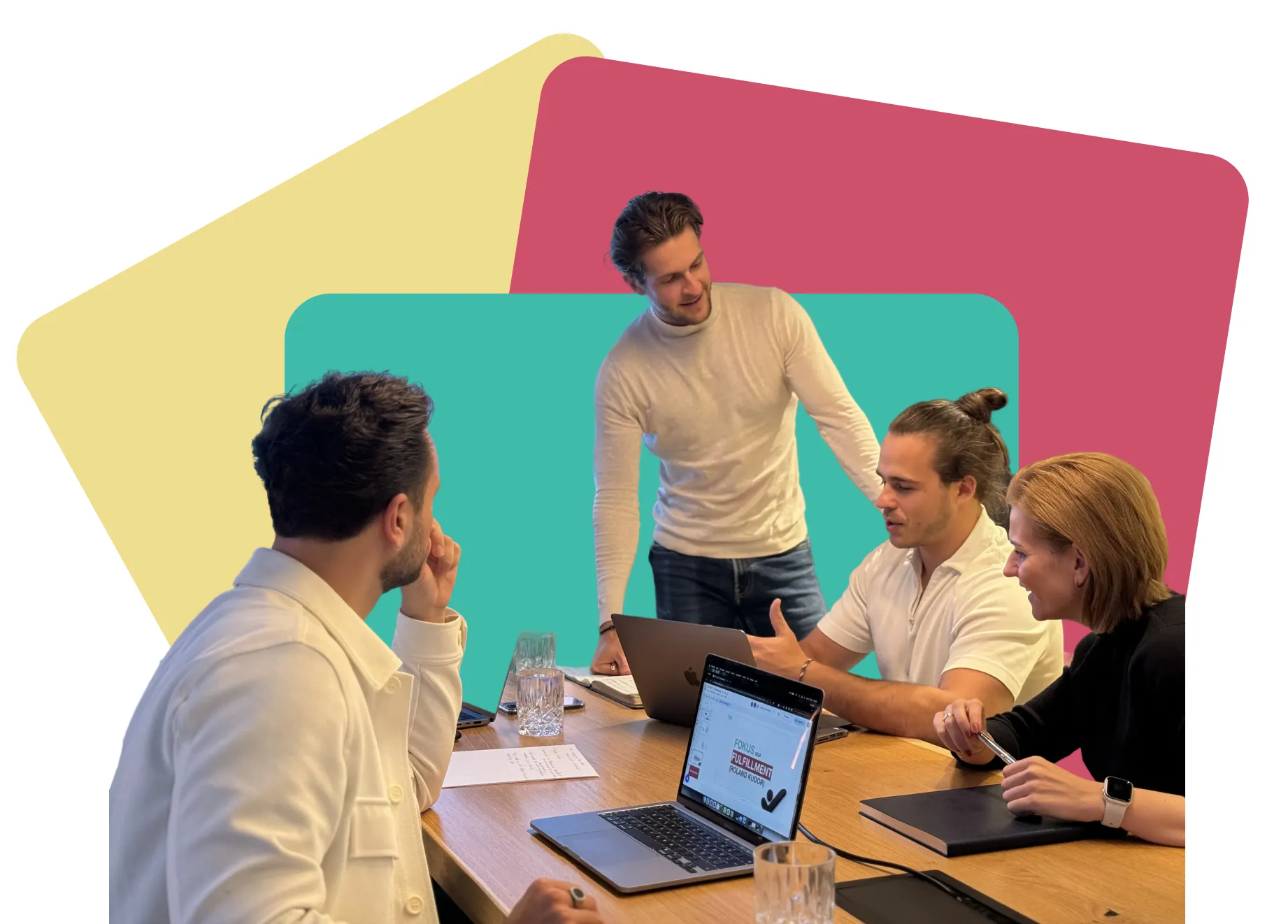 Vier Kollegen diskutieren bei einem Meeting um einen Tisch mit Laptops und Notizbüchern.