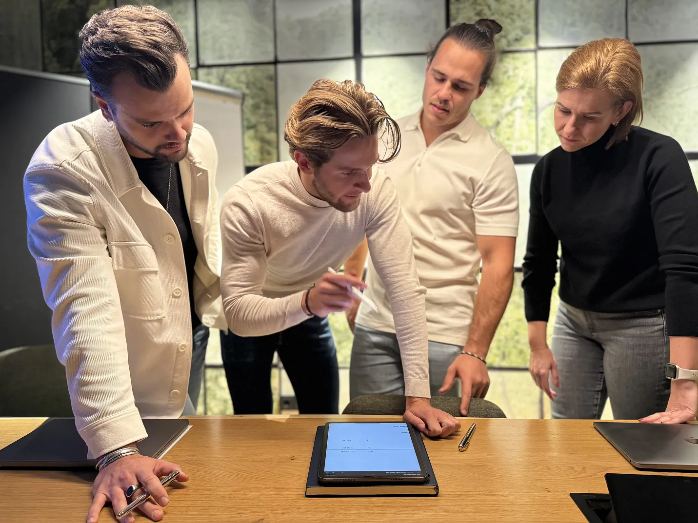 Vier Personen arbeiten gemeinsam an einem Tablet auf einem Holztisch im Büro.