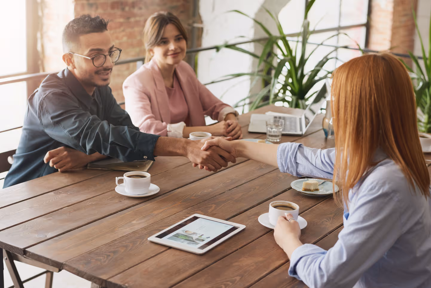 A diverse team of professionals collaboratively working with a client at a table, utilizing a tablet for efficient communication and project management.