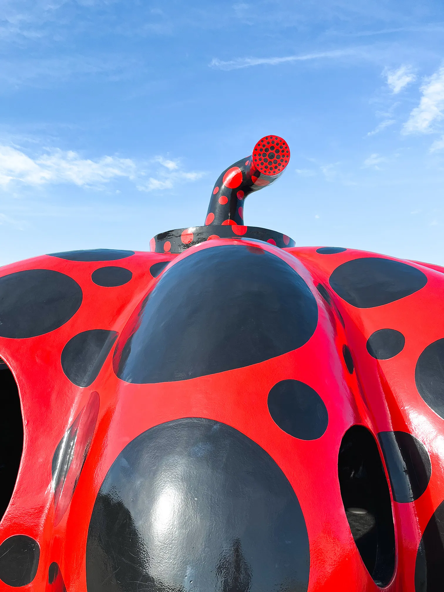 Close-up of a large red sculpture with black polka dots resembling a ladybug under blue sky.
