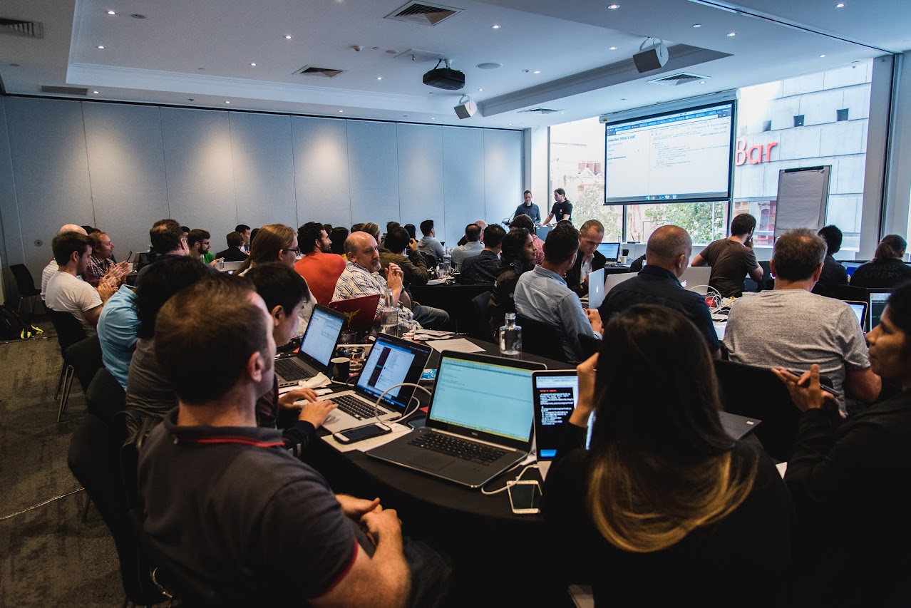 A room of professionals with laptops at a workshop on software development with Rick Giner behind a lectern at the front