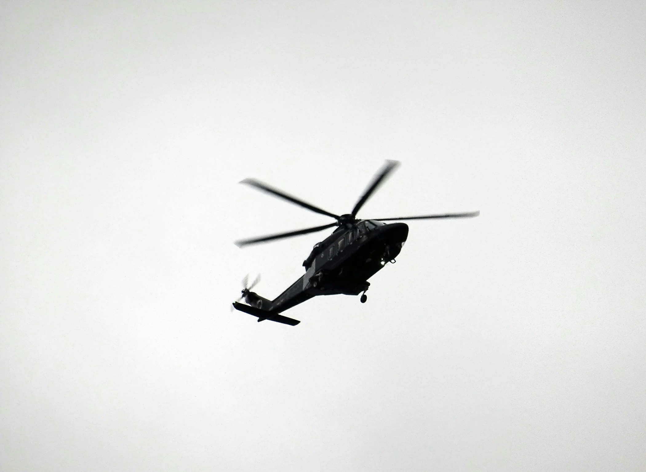 Silhouette of a helicopter flying against a light gray sky.