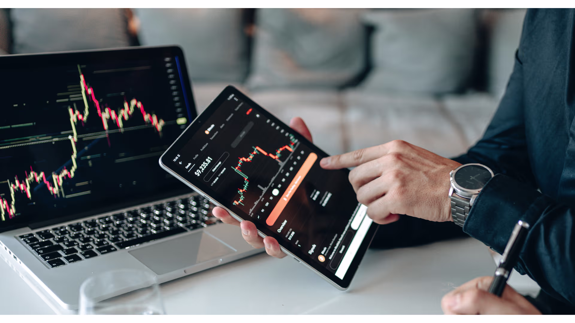 A person analyzes financial charts on a laptop and tablet, reviewing market trends and investment data.