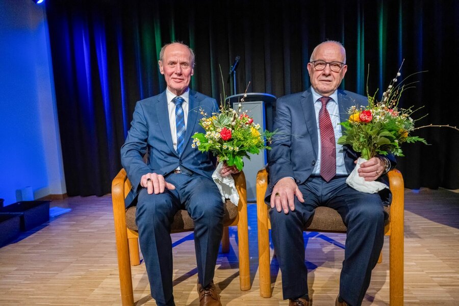 Bild vergrößern: Zwei Männer sitzen mit Blumensträußen auf einem Sessel.