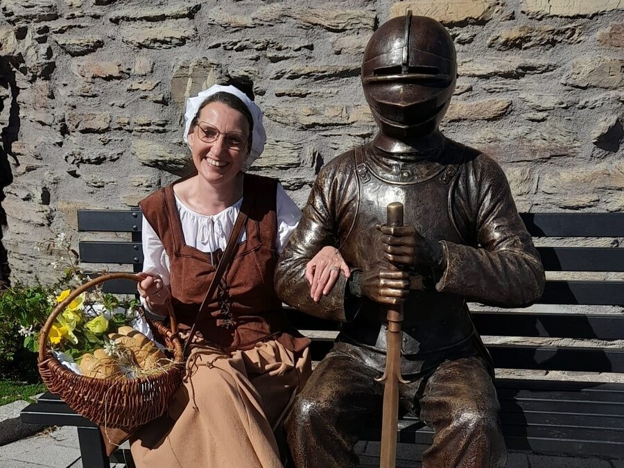 Bild vergrößern: Eine historisch gekleidete Marktfrau neben einer Statue.
