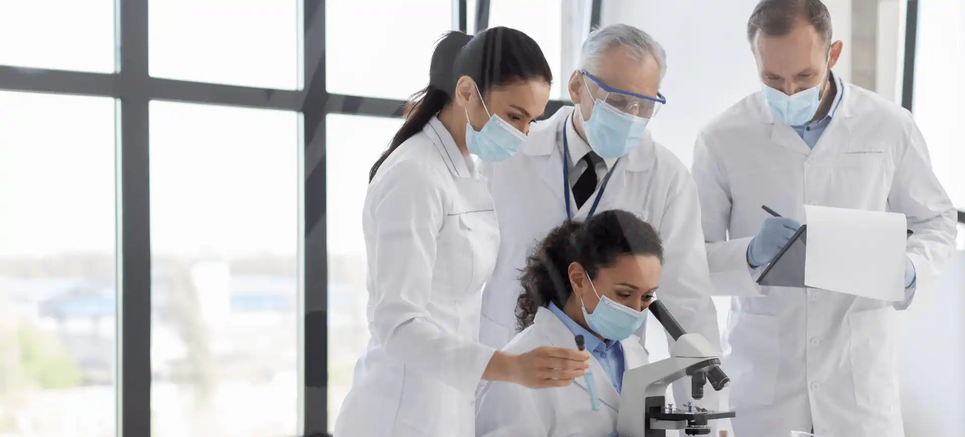 A group of people in white lab coats looking through a microscope