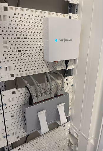 Weiße Elektronik mit Viessmann-Logo und sechs graue Netzwerkkabel, die in einen grauen Netzwerk-Switch eingesteckt sind.