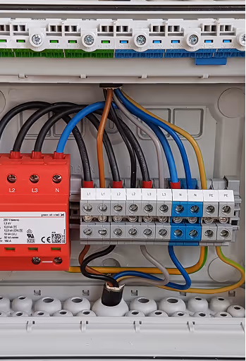 Elektrischer Anschlusskasten mit beschrifteten Klemmen L1, L2, L3, N, PE und verschiedenen schwarzen, blauen, gelben und braunen Kabeln.