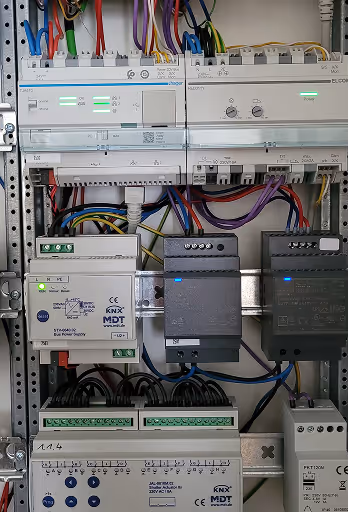Steuerungspanel mit beschrifteten elektrischen Komponenten, zahlreichen farbigen Kabeln und leuchtenden LEDs in einem Schaltkasten.