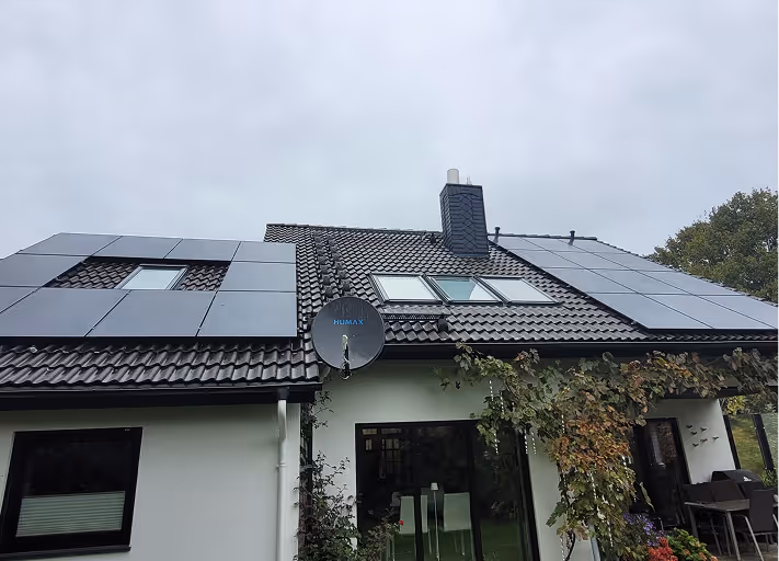 Haus mit dunklem Ziegeldach, mehreren Sonnenkollektoren und einer HUMAX Satellitenschüssel an der Dachkante.