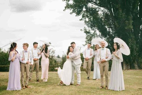 Mia and Joe embracing in the middle of the wedding party on a grassy field under big trees
