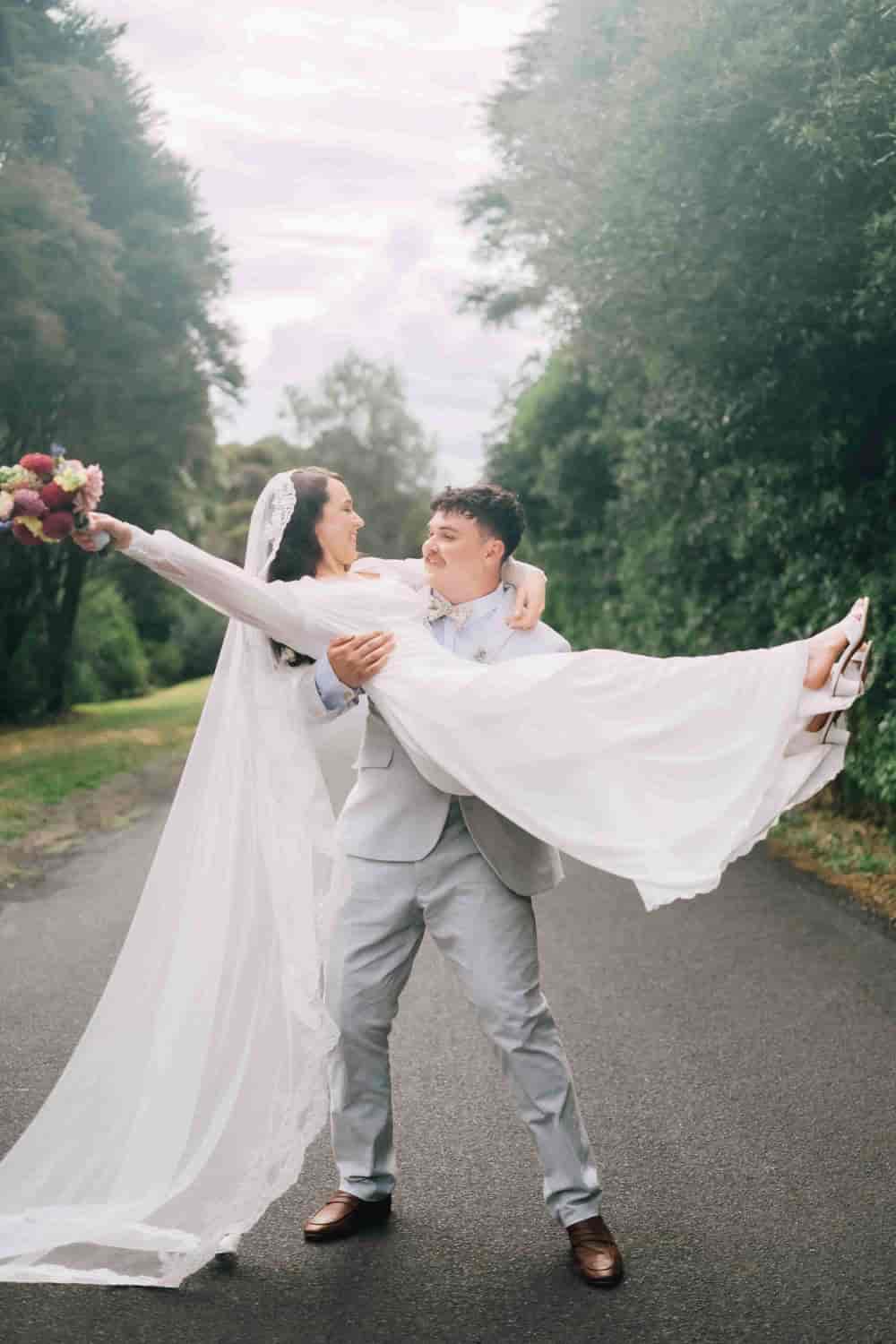 Joe lifting Mia off her feet on a country road, her bouquet held high and veil flowing