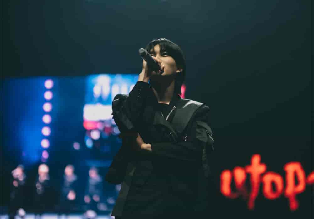 P1Harmony member in black singing into a microphone, the glowing UTOP1A logo on the screen behind
