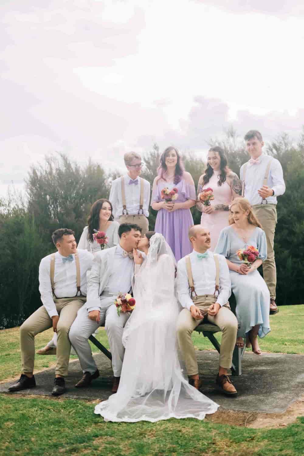 Mia and Joe touching noses in the middle of their seated wedding party on a grassy rise