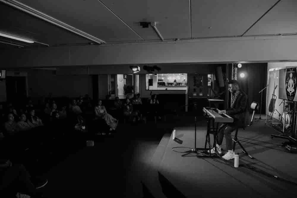 Wide, very dark black and white view of the hall with Josh alone at a keyboard and a seated audience