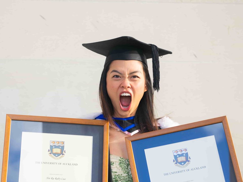 Ruby shouting with excitement in her graduation cap, holding two University of Auckland degrees