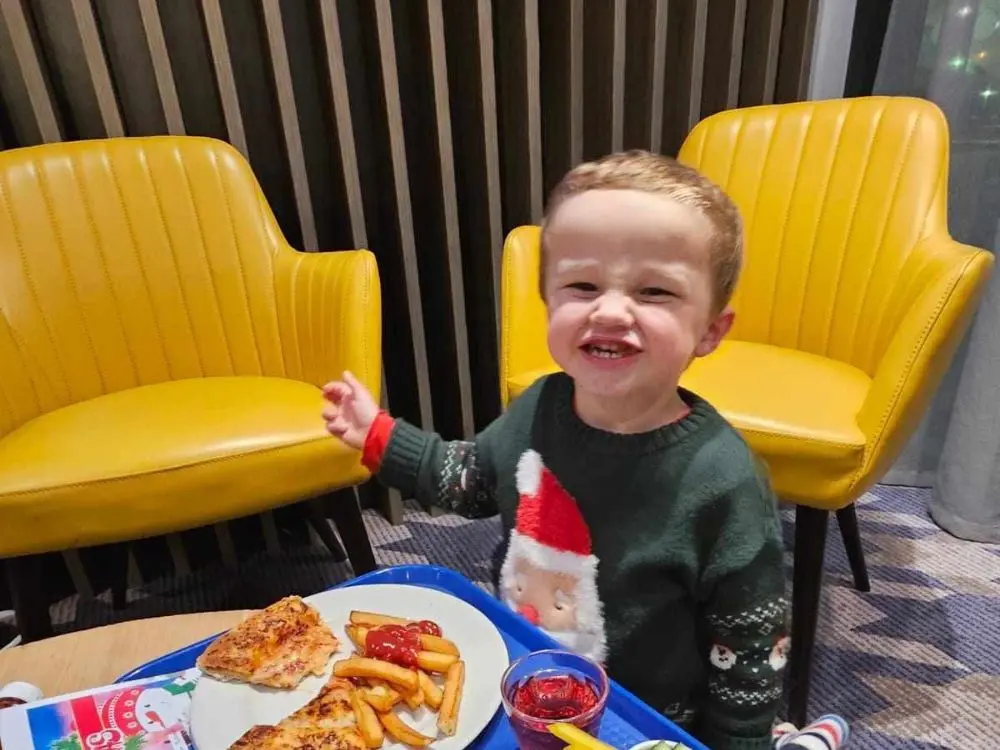 young boy in a Santa jumper smiling happily while enjoying a festive meal of pizza and chips.