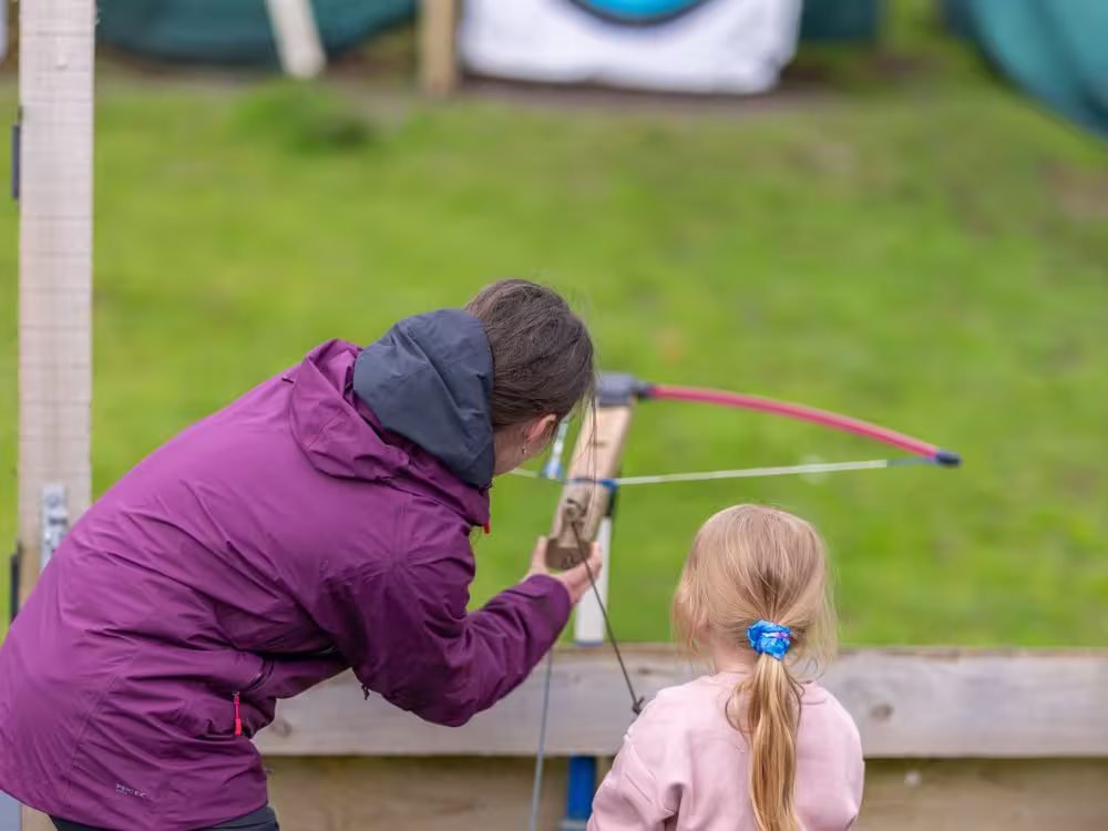 An adult helping a young girl aim a crossbow during an archery session at Calvert Lakes