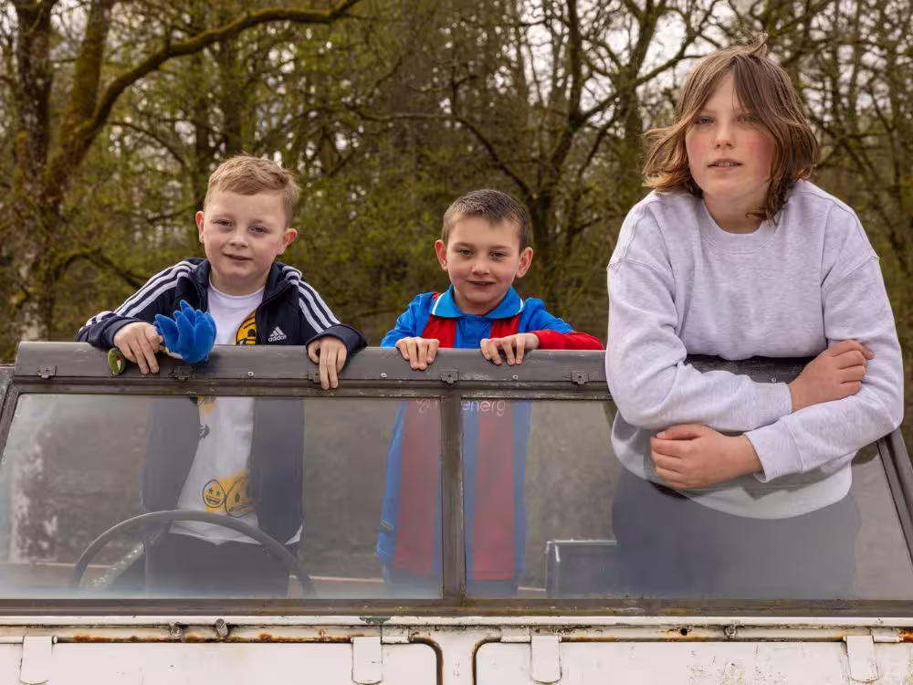 Three children leaning over the roof of an old Land Rover at Calvert Lakes, smiling at the camera