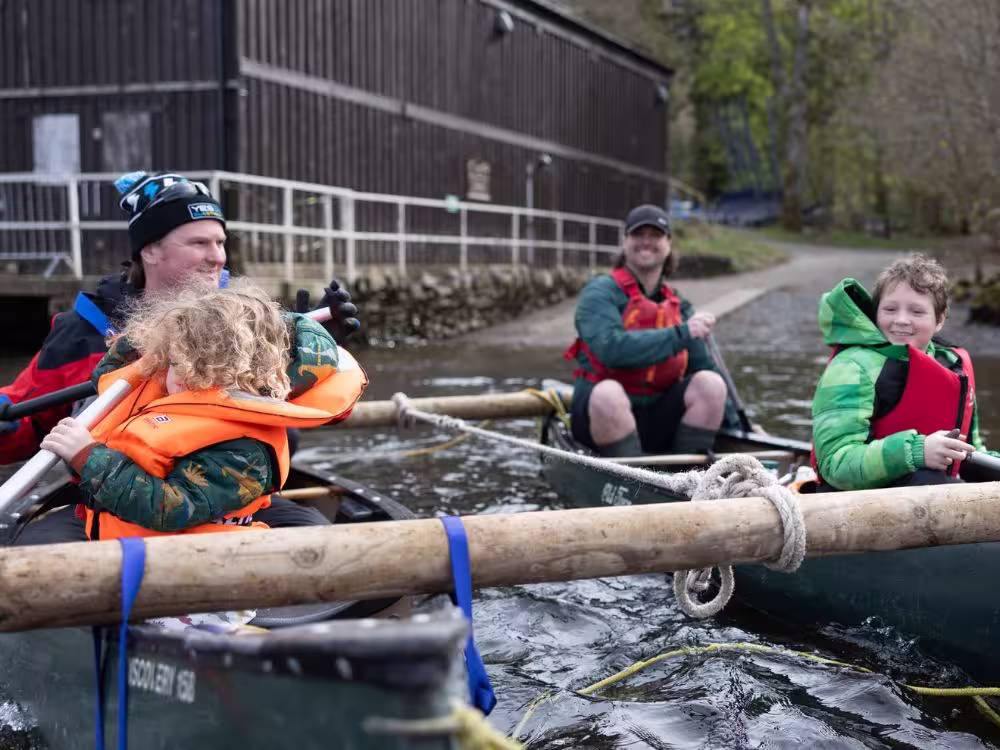 Two adults and two young children smiling in canoes at Calvert Lakes, with the children wearing orange and red life jackets