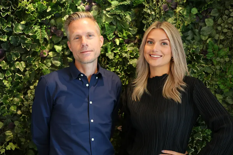 En man och en kvinna står framför en vägg iklädd gröna växter.