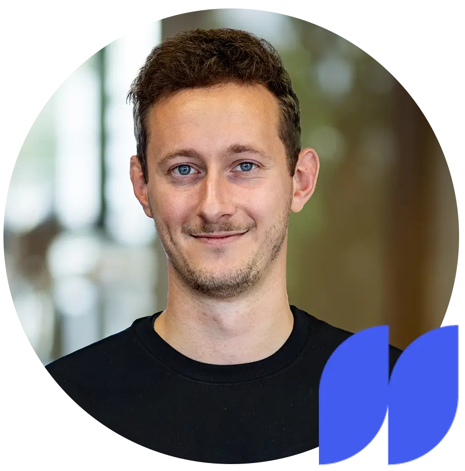 Porträt eines lächelnden Mannes mit kurzem braunem Haar und blauem T-Shirt vor unscharfem Hintergrund.