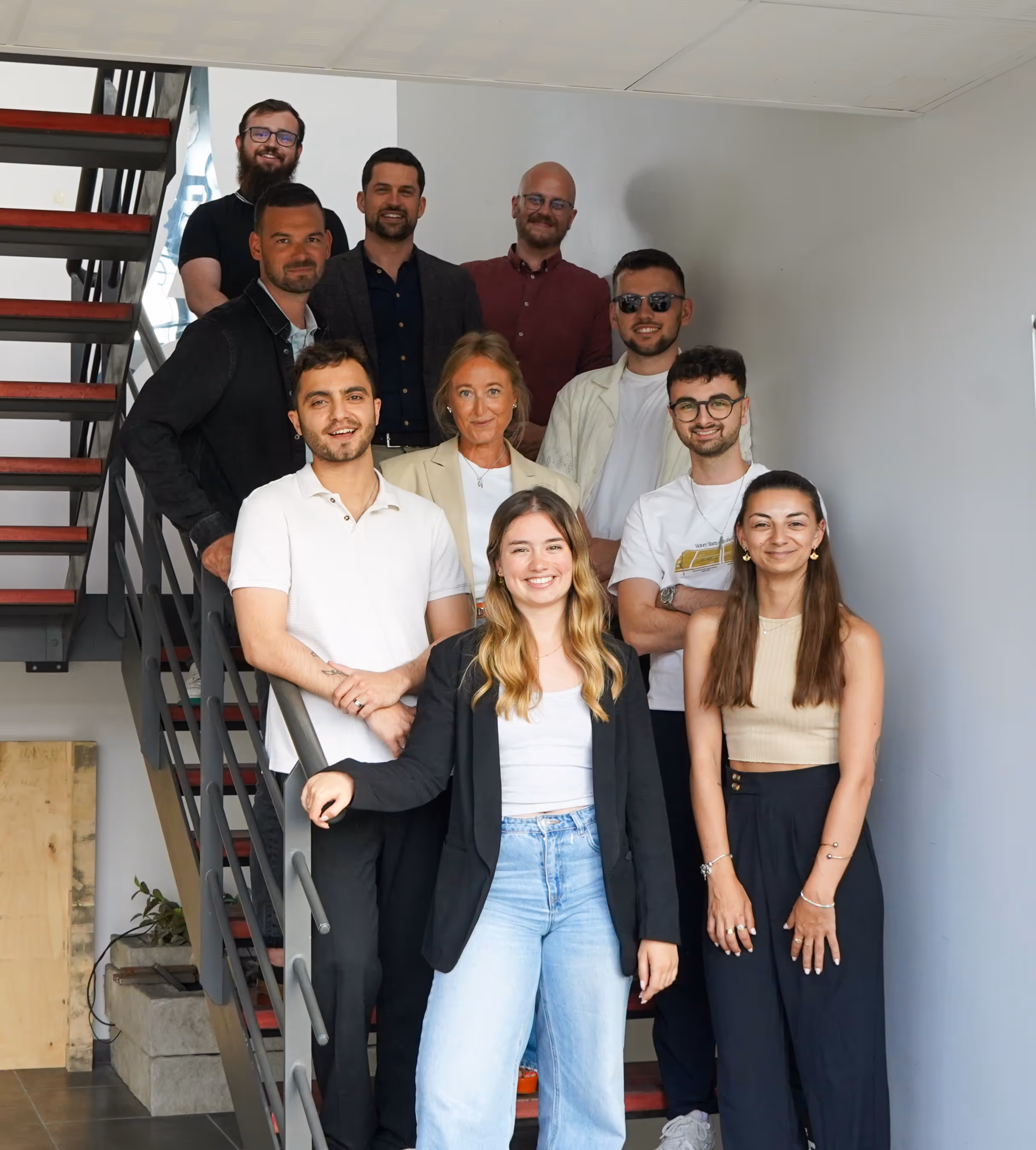 Groupe de onze jeunes adultes souriants posant sur un escalier intérieur moderne.