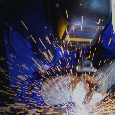 Person using a welder with gloves and welding helmet on, sparks flying