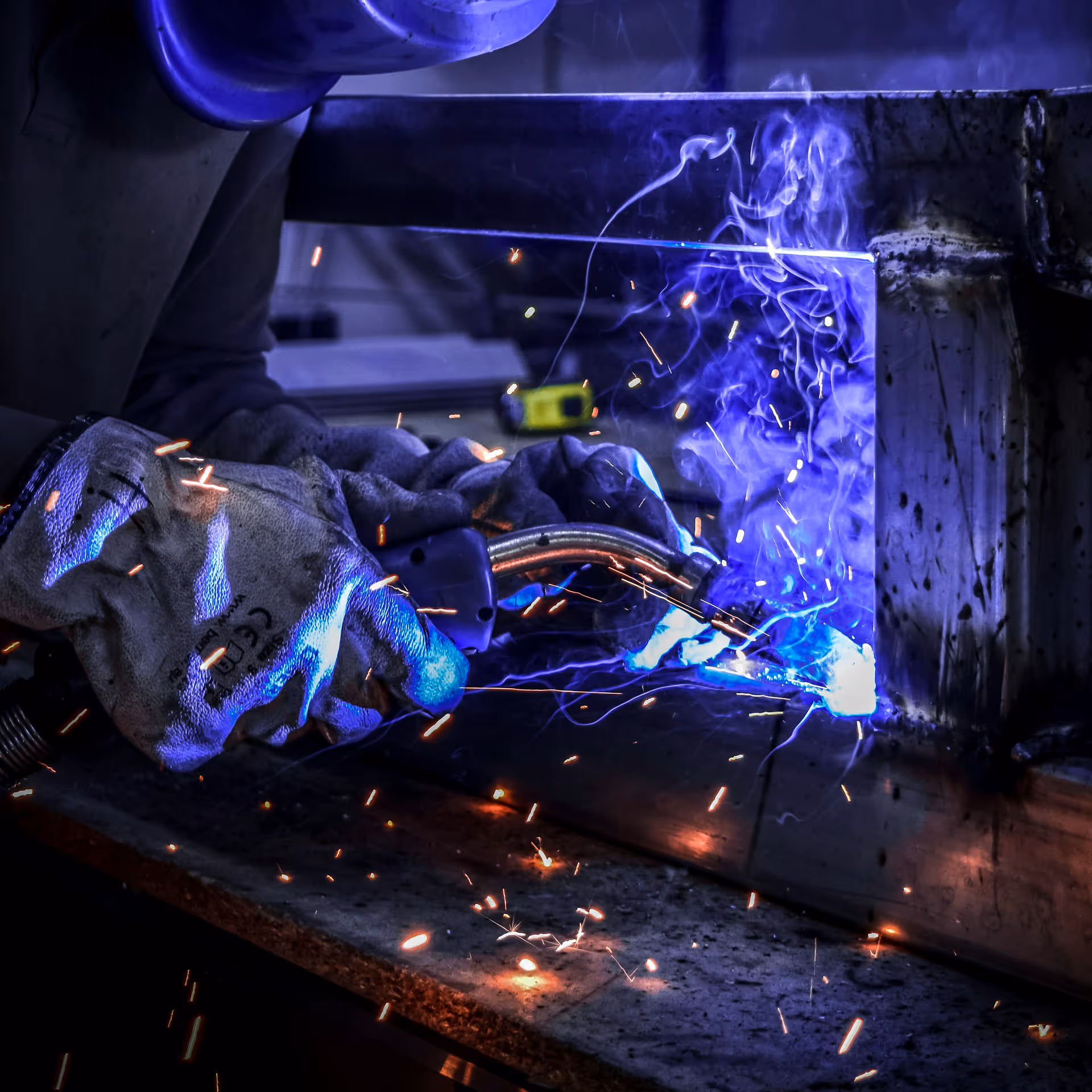 Welding torch welding metal creating blue light and and sparks.