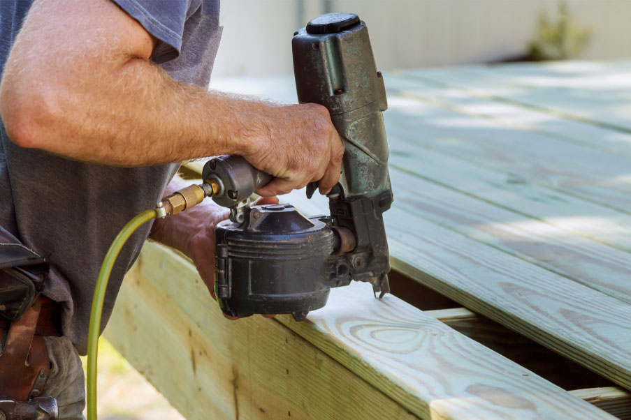 A nail gun putting nails in wood decking.