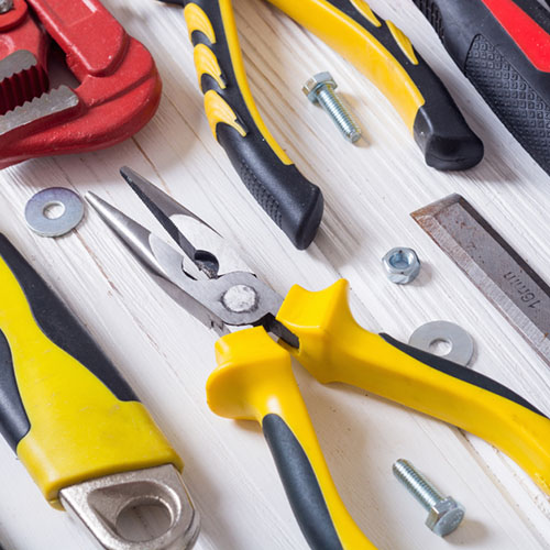 A pair of yellow pilers surrounded by other tools, bolts and washers.