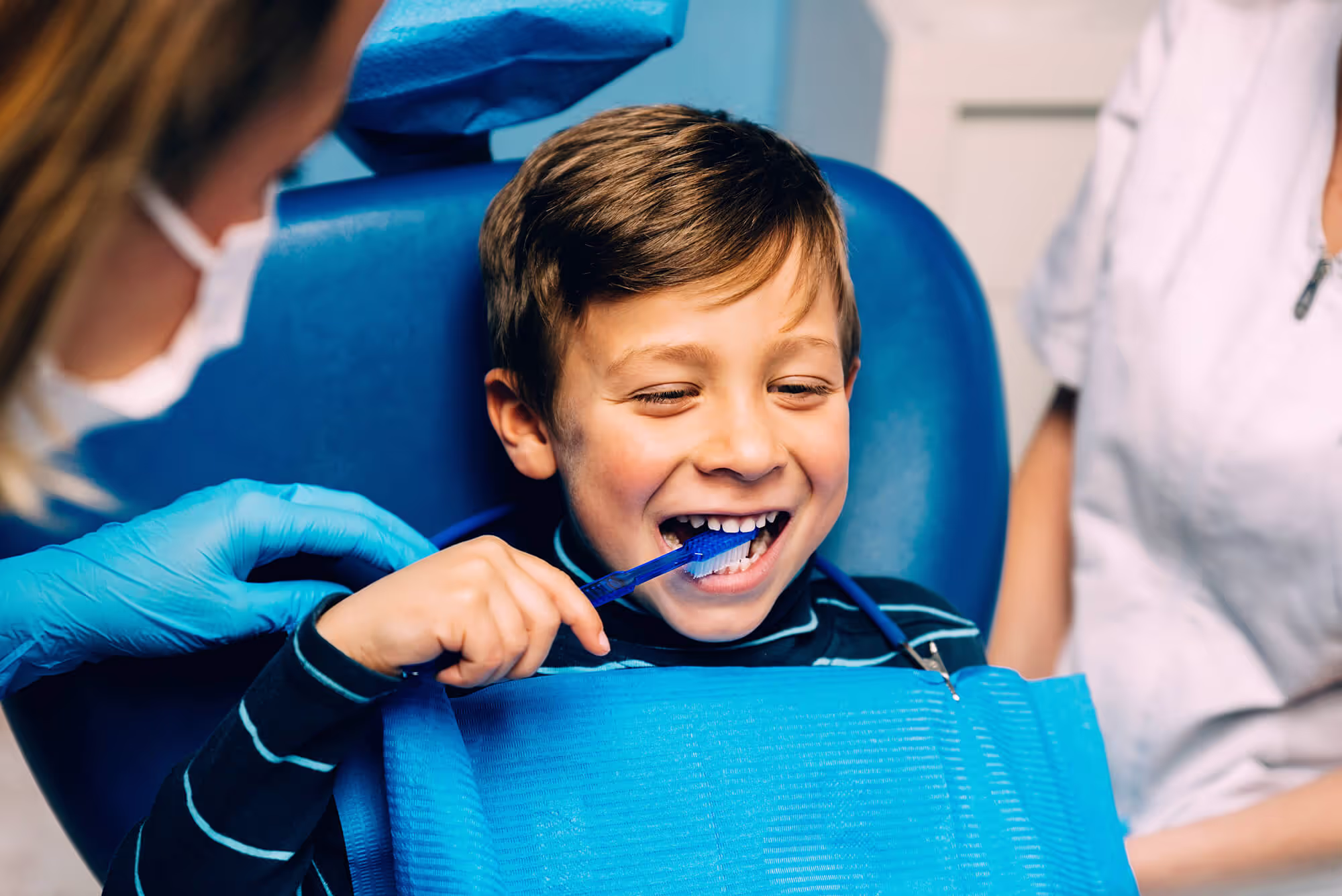 A young boy getting his teeth brushed by a dentist.