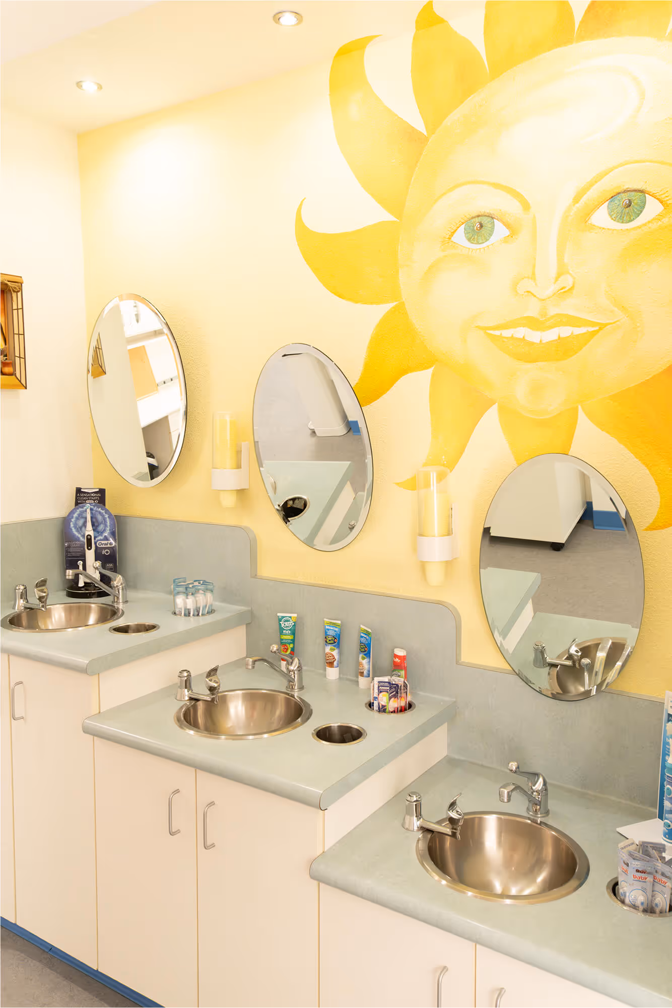 A bathroom with three sinks and a sun painted on the wall.