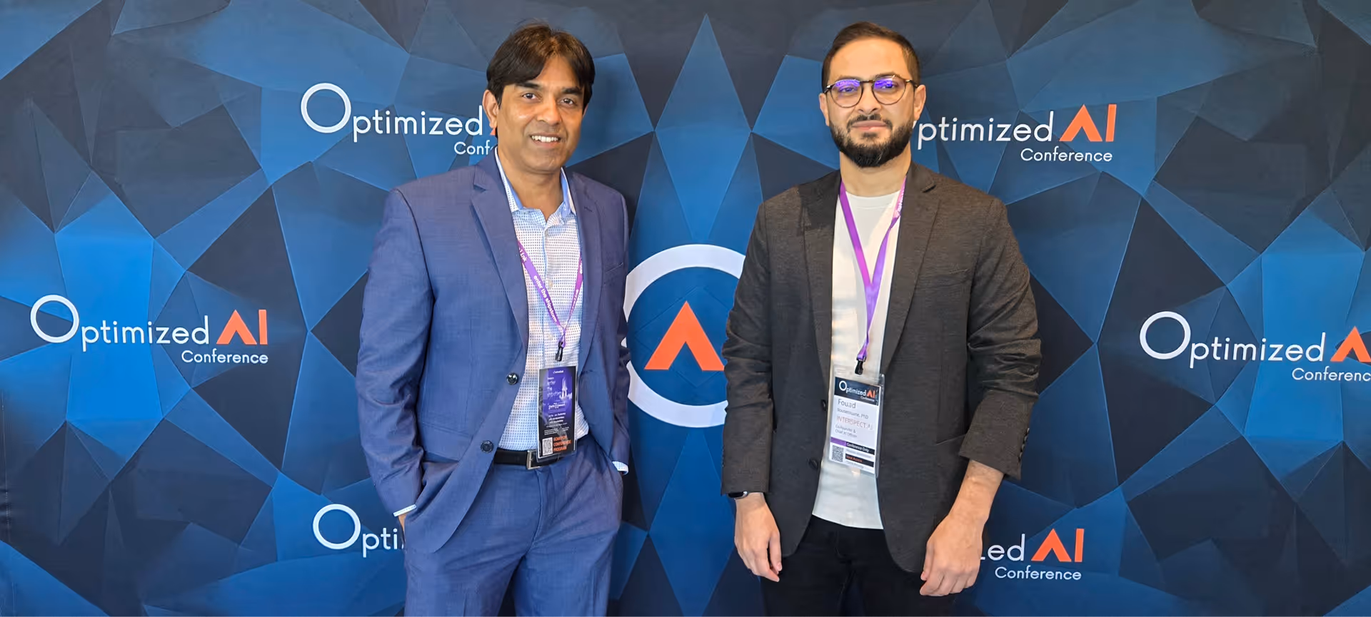 InterspectAI’s cofounders at the OptimizedAI conference standing in front of an OptimizedAI branded screen