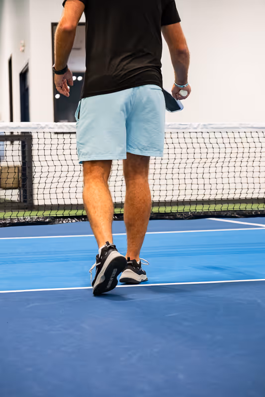 A man walking on a blue pickleball court.