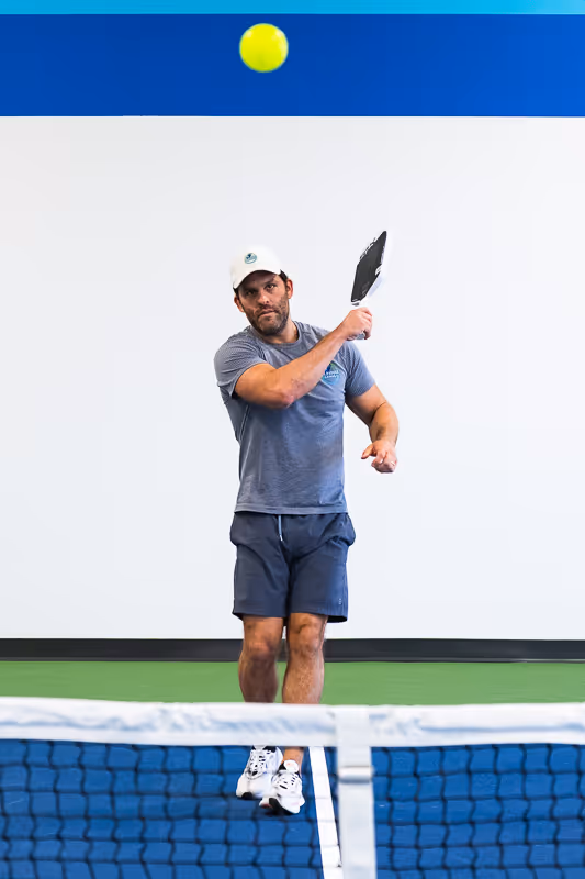 A man striking a pickleball in an indoor pickleball facility.