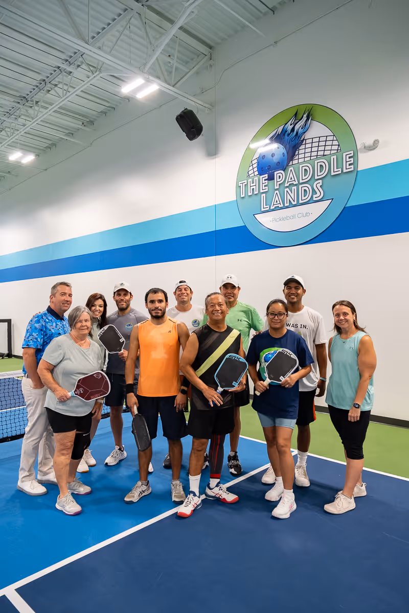 A group of pickleball players posing for a photo in front of the logo for The Paddle Lands.