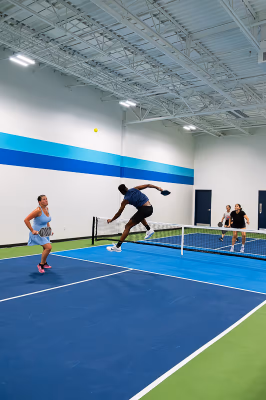 A pickleball player jumping in the air to hit a ball that was lobbed over his head.