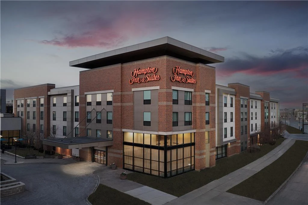 Exterior view of a Hampton Inn & Suites hotel building at dusk with illuminated signage.