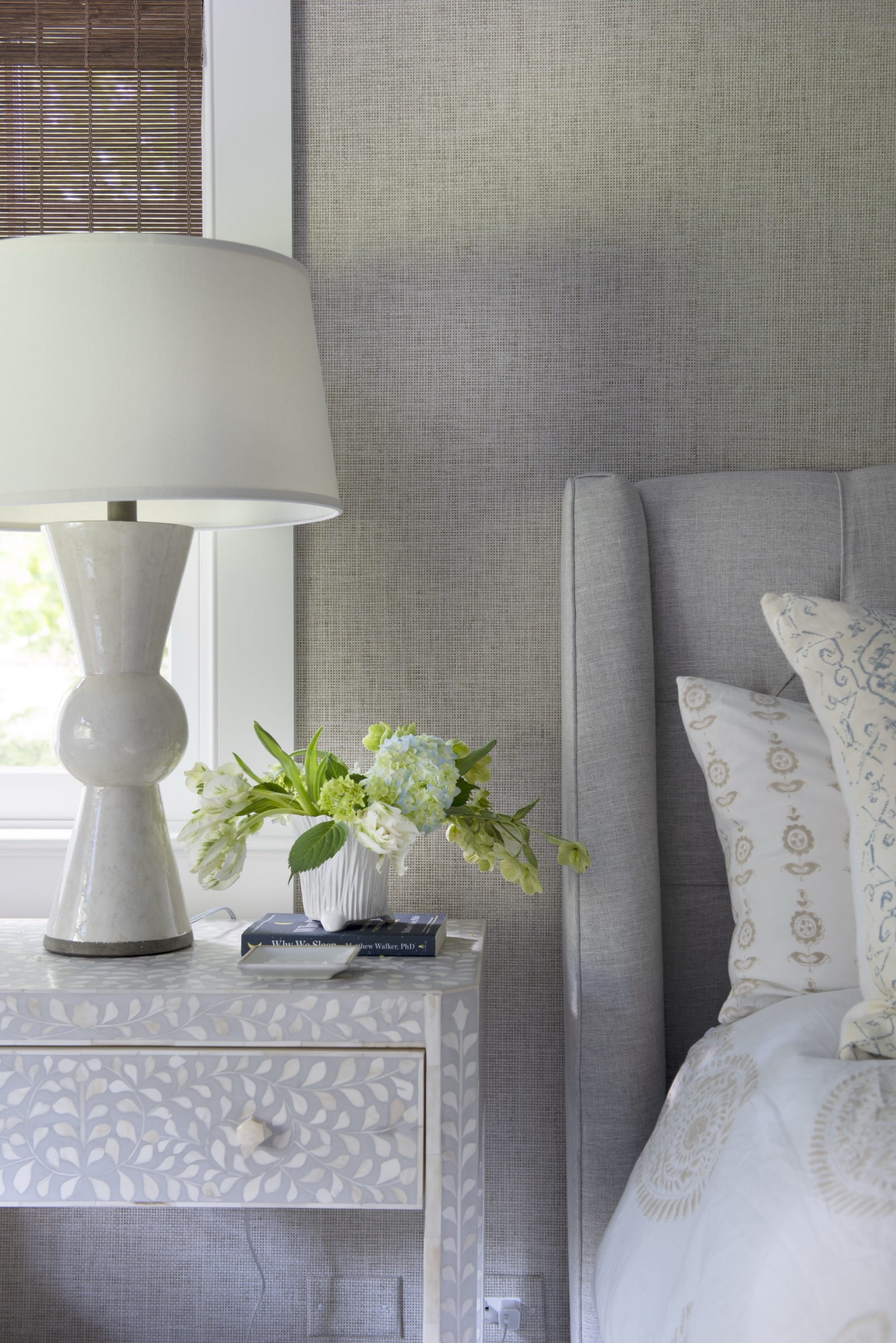 Nightstand with white lamp beside bed.
