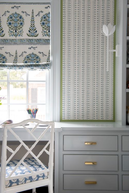 Built-in desk with white drawers and window shade.