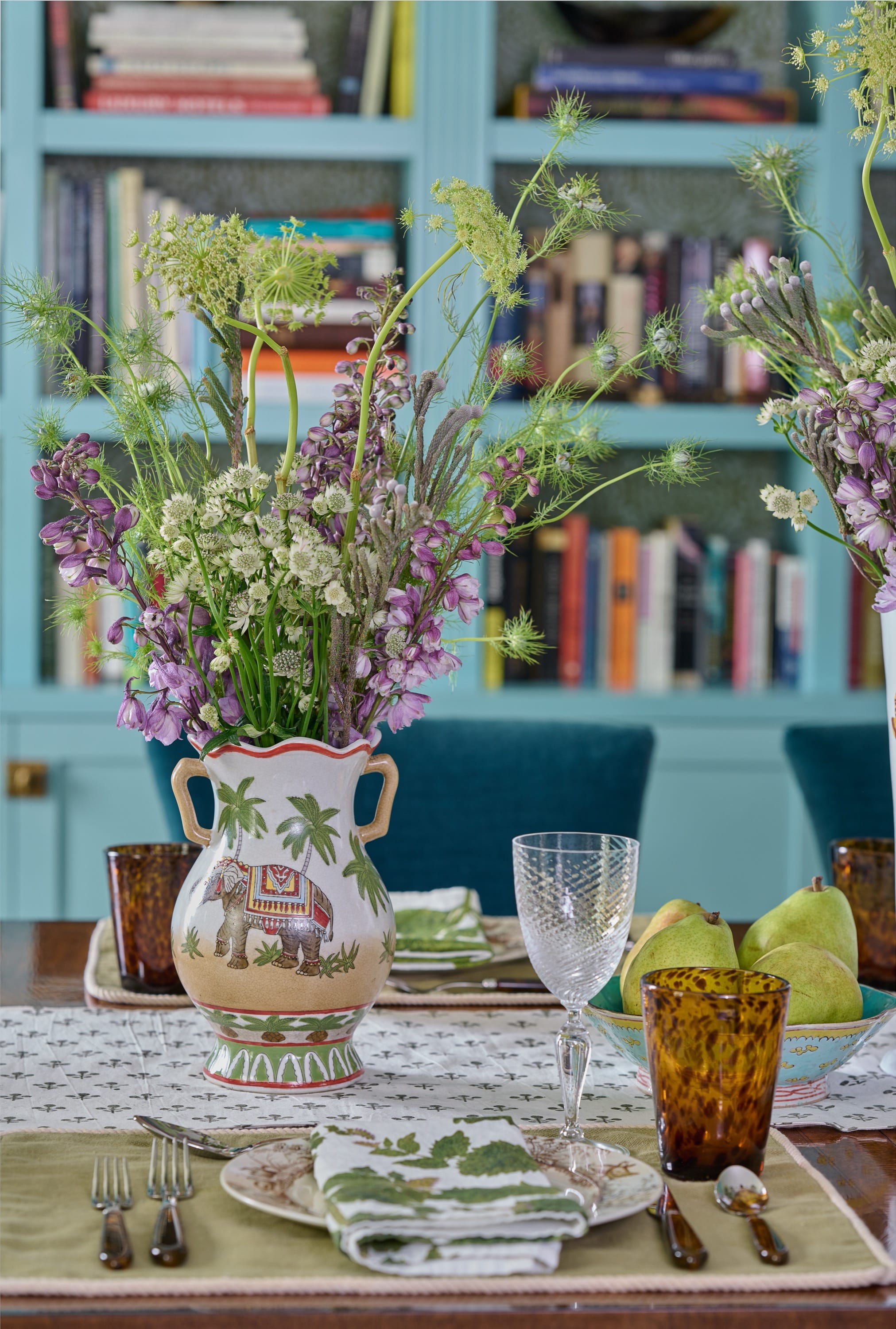 Table set with flowers, glassware, and bookshelves.