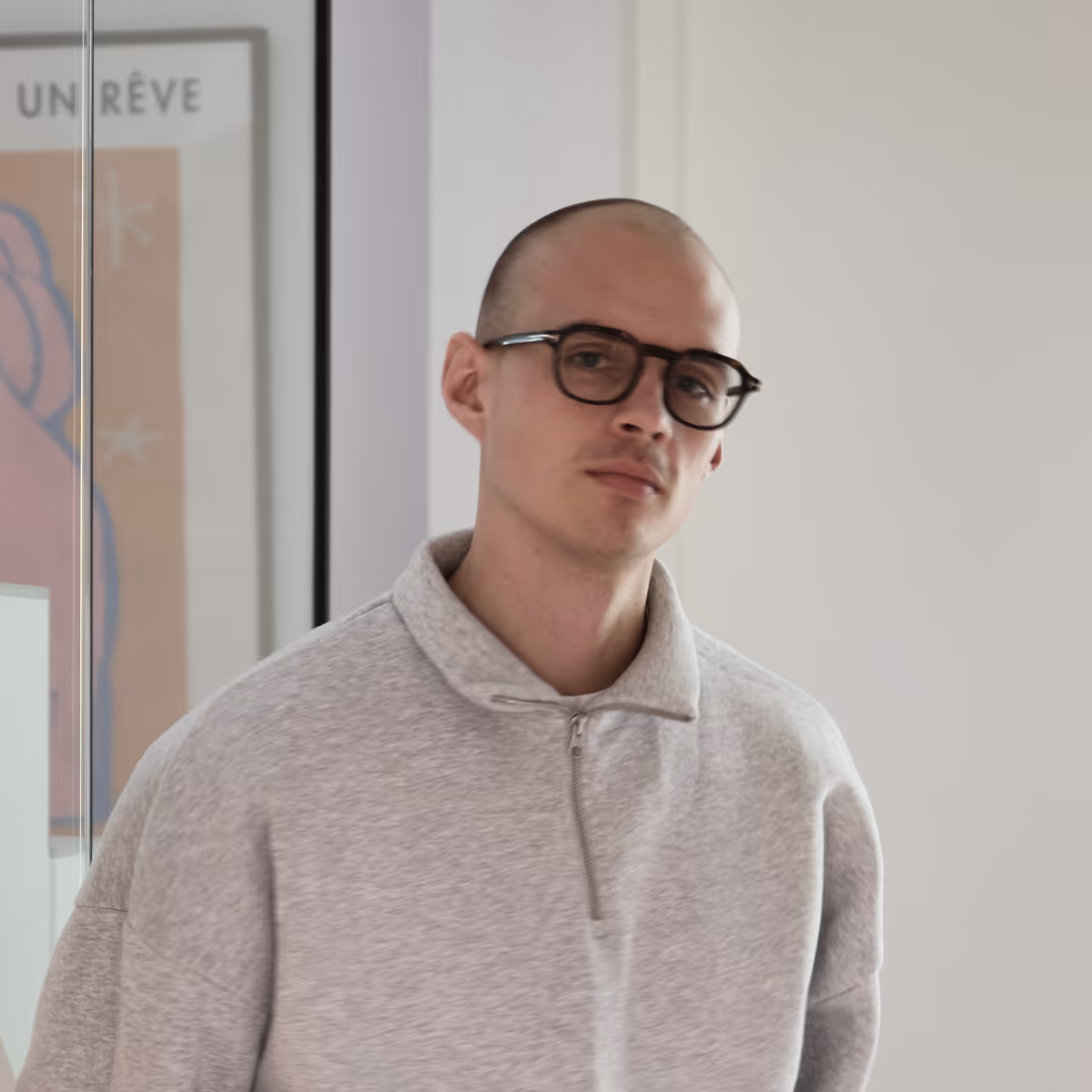 Jonge man, Leander Haesaert, met een grijze trui en een bril, staand in een neutrale binnenruimte.