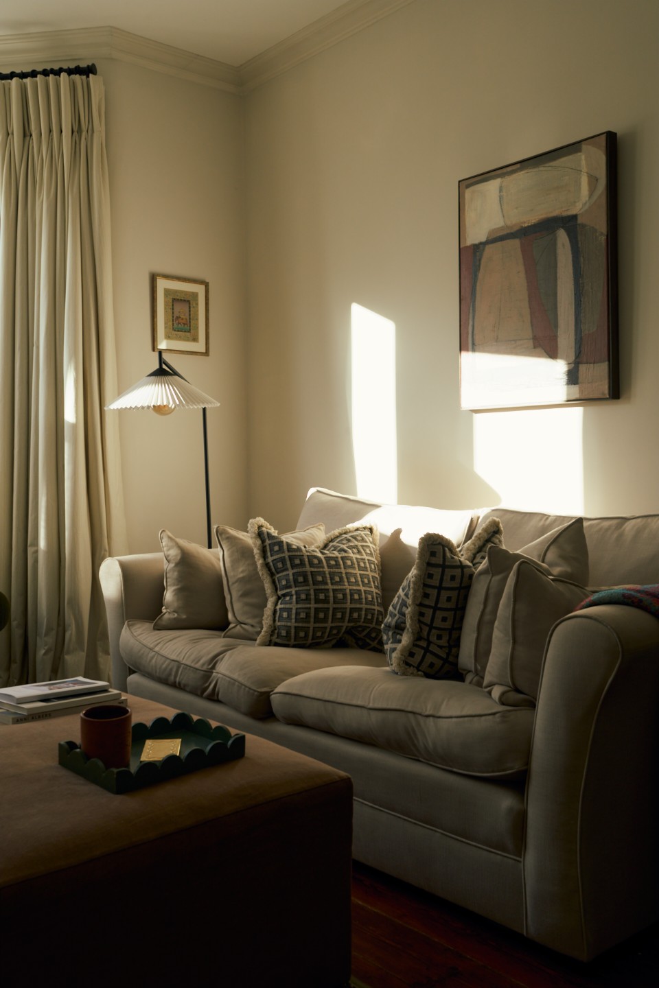 Photo of the interior of a living space, focusing on the sofa. There's a coffee table in front, an art piece on the wall behind and a lamp on the side. Designed by Spratley & Partners.