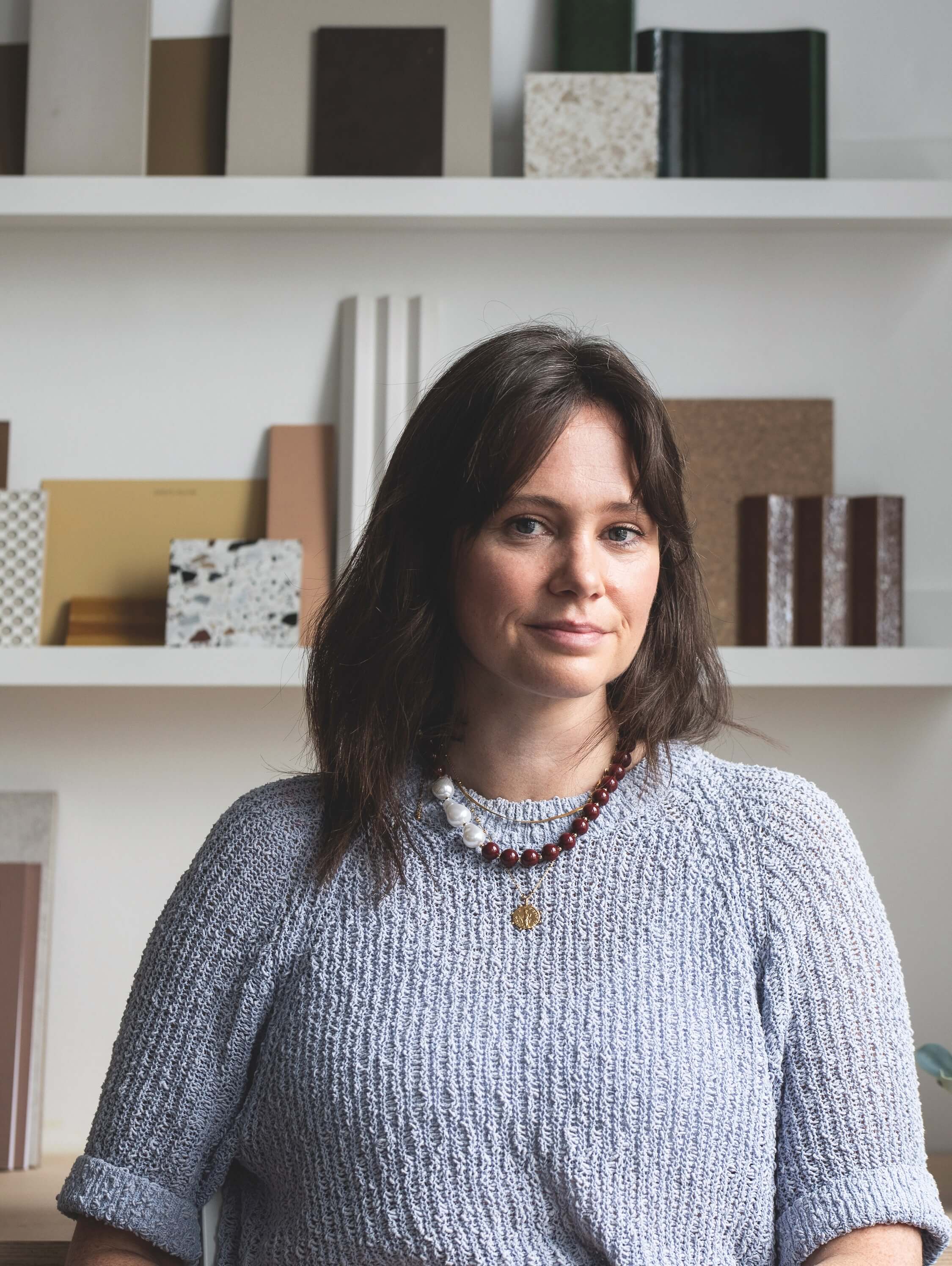 Portrait photo of Louise Hawes Baker, an architect and Head of Interior Design at Spratley & Partners, with a bookshelf behind her filled with material samples.