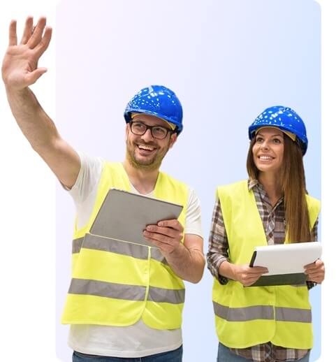 Two construction workers wearing blue hard hats and yellow safety vests smile.