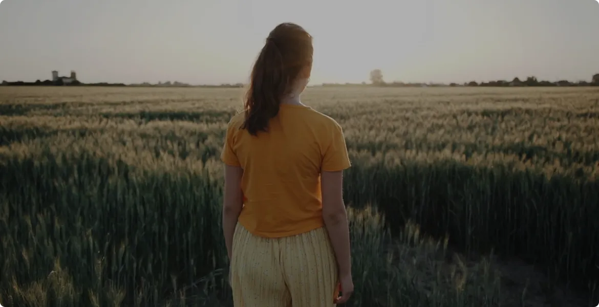 A girl looking at a green field on a sunny day.