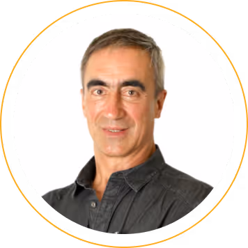 Portrait of a middle-aged man with short gray hair wearing a dark collared shirt, smiling slightly against a white background.