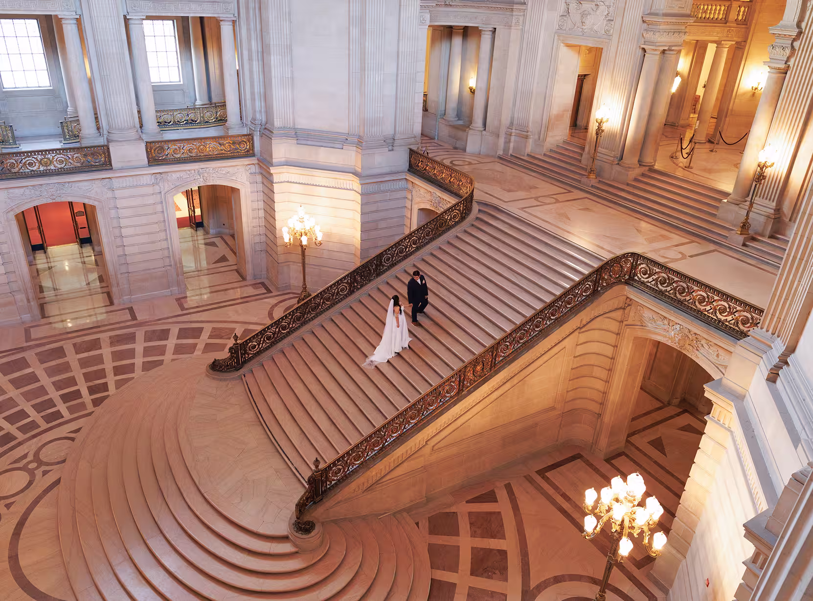Bride and groom walking down the grand staircase at San Francisco City Hall, elegant wide-angle wedding portrait with marble architecture and warm light